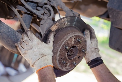 Brakes Repair in Kenner, LA by CAMS Automotive. Image of a man’s hands removing the worn brake disc from the rear wheel hub.