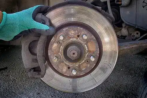 Why Brake Pads and Rotors Should Be Replaced Together | CAMS Automotive ib Kenner, LA. Image of a mechanic’s hand holding a brake pad attached to a brake rotor without wheels.