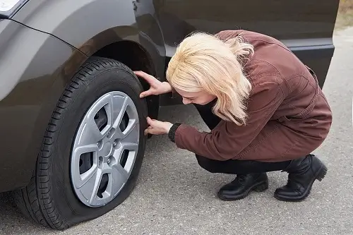 The Essential Pre-Trip Vehicle Inspection for the Holidays | CAMS Automotive in Kenner, LA. Image of a woman checking her flat tire.