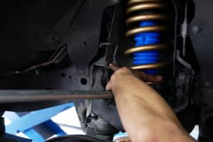 Signs Your Vehicle Needs New Shocks or Struts: Expert Insights. Close up image of mechanic hands and arms working on shocks on car in shop.