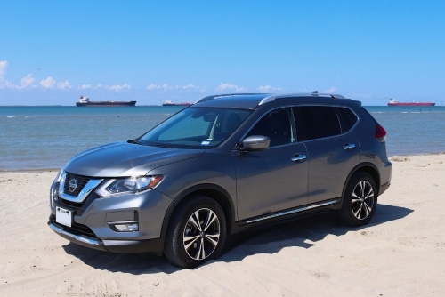 Nissan repair and maintenance services in Kenner, LA at CAMS Automotive. Image of gray Nissan Rouge SUV on beach with the gulf of Mexico in the background with four barge ships.