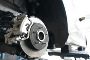 routine car maintenance, auto repair in Kenner, LA at CAMS Automotive. Image of a close-up view of a car’s disc brake and caliper on a lift.