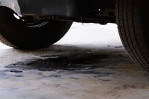 Car fluid leak, auto repair in Kenner, LA by CAMS Automotive. Image of dark engine oil pooling beneath a vehicle’s undercarriage, highlighting active fluid leaks that require prompt inspection to protect engine performance and prevent costly damage.