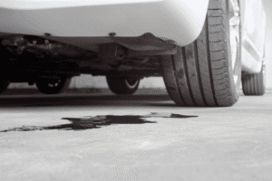 Car fluid leak, auto repair in Kenner, LA at CAMS Automotive. Image of dark fluid pooled beneath a white vehicle, indicating a leak that should be diagnosed to support reliable operation.