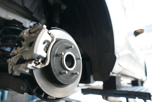 CAMS Automotive – routine services routine car maintenance, auto repair in Kenner, LA at CAMS Automotive. Image of a close-up view of a car’s disc brake and caliper on a lift.